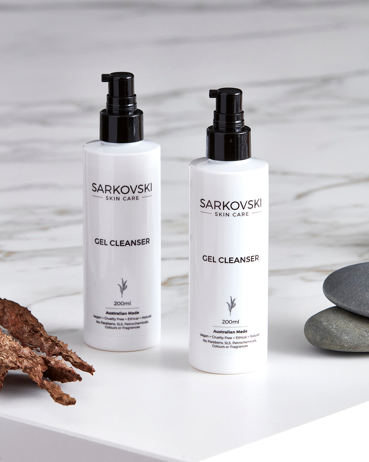 SARKOVSKI Gel Cleanser bottles on a cemented surface, with rustic bark and stone on both sides, emphasizing its natural ingredients and hydrating formula.