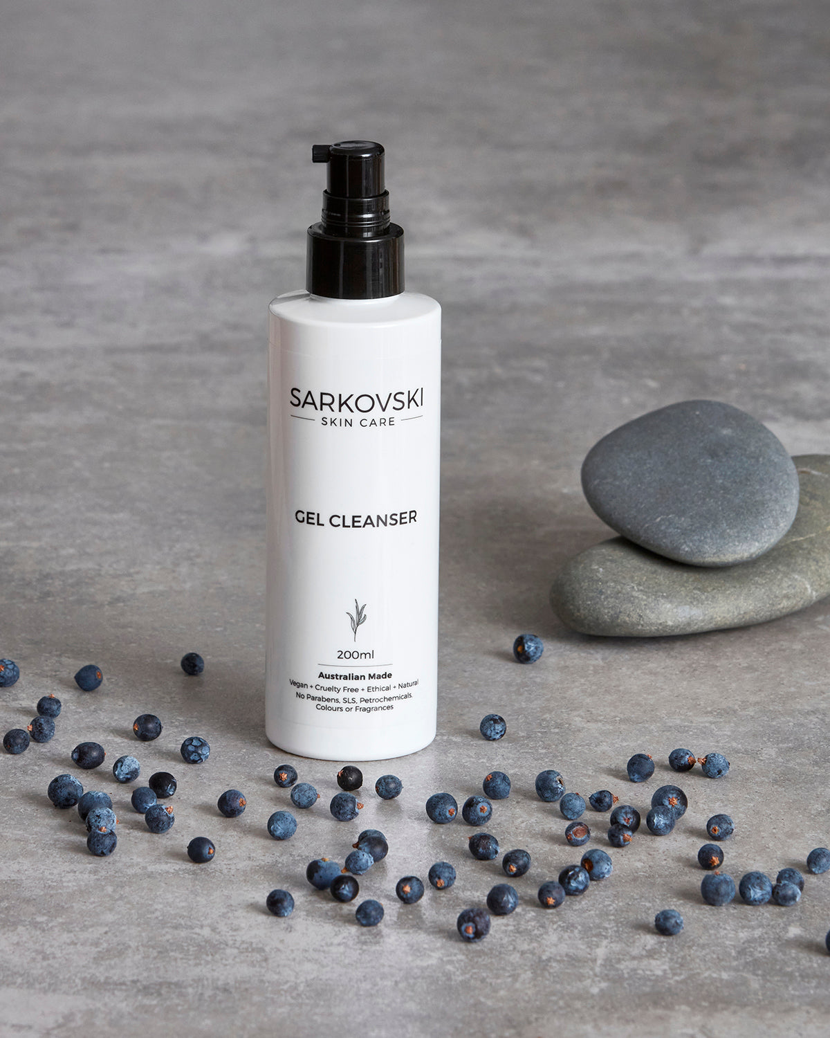 a photo SARKOVSKI® Gel Cleanser - Australian-made with antibacterial juniper berry and lime essential oils designed for oily and acne-prone skin. A Sleek bottle with juniper berries neatly arranged on top of marble table.