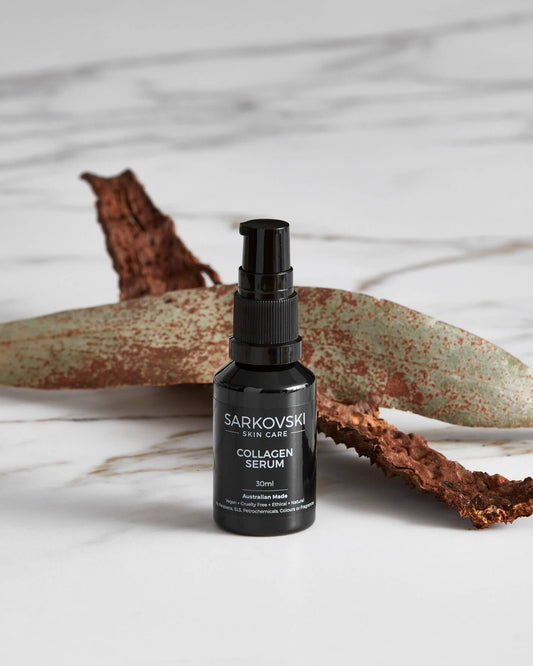 SARKOVSKI® Skin Care Collagen Serum bottle with a sleek design in a black pump bottle with wooden bark on top of marble. Collagen Serum designed to boost collagen, hydrate deeply, and restore skin elasticity.